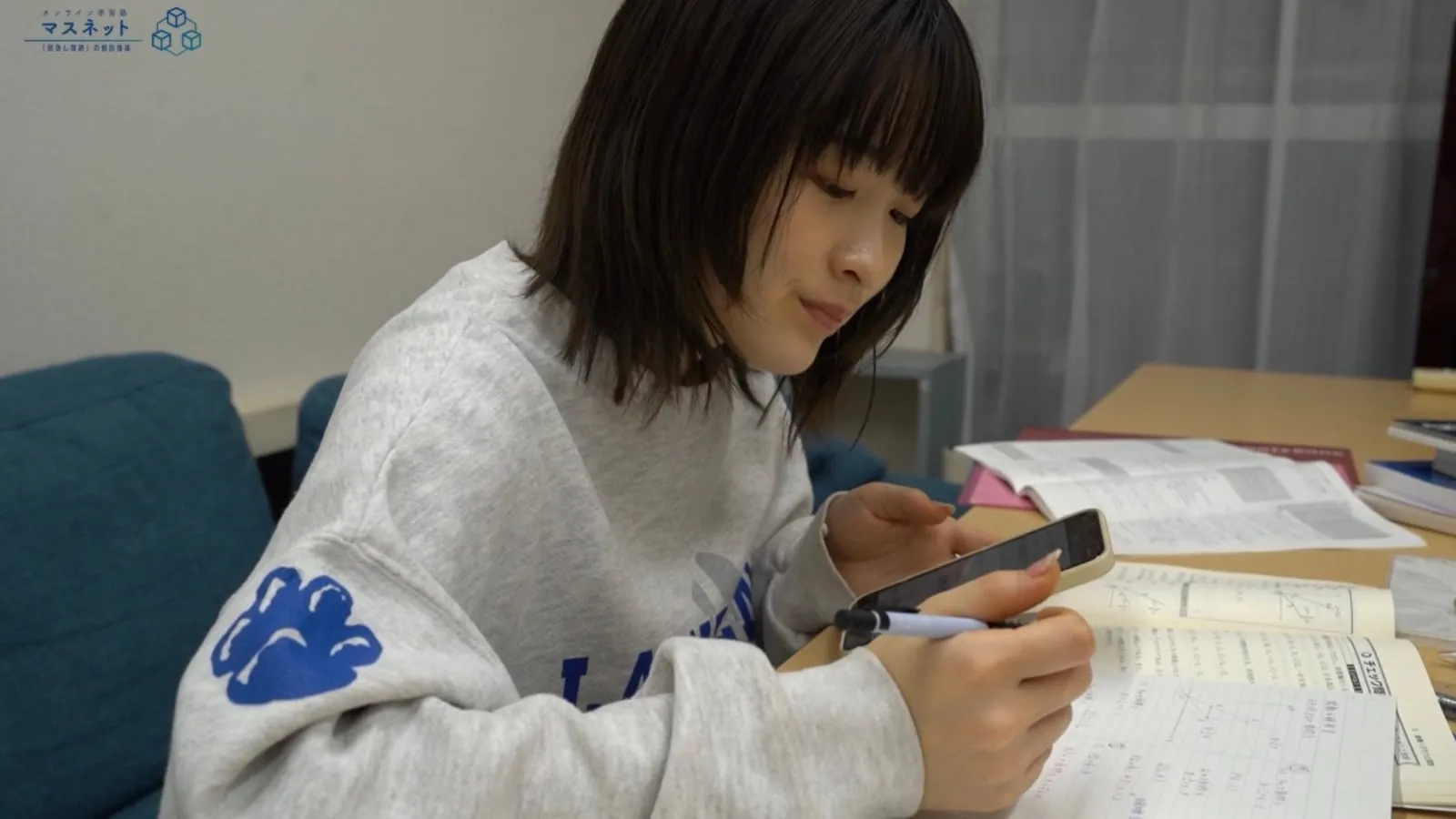 自宅の机で参考書とスマートフォンを使って学習する生徒